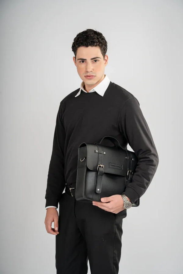 Man holding a black leather backpack against a gray background