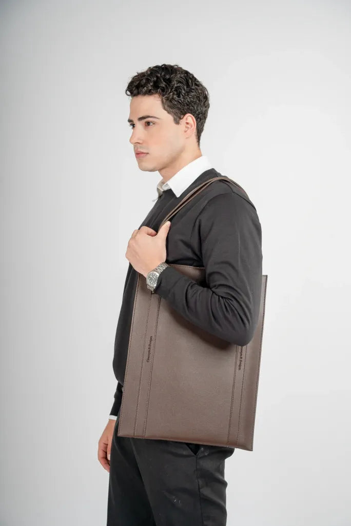 Man holding a brown leather bag against a white background
