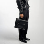 Person holding a black leather satchel bag with a visible brand logo.
#color_midnight