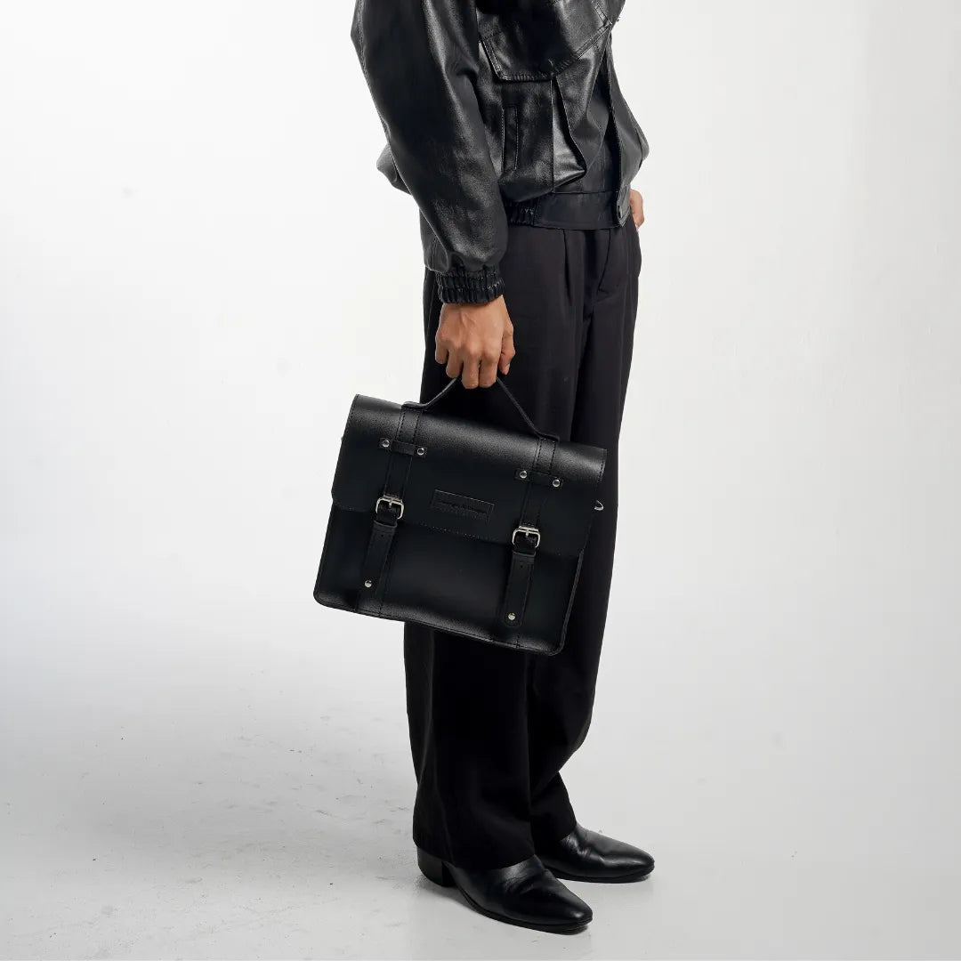 Person holding a black leather satchel bag with a visible brand logo.
#color_midnight