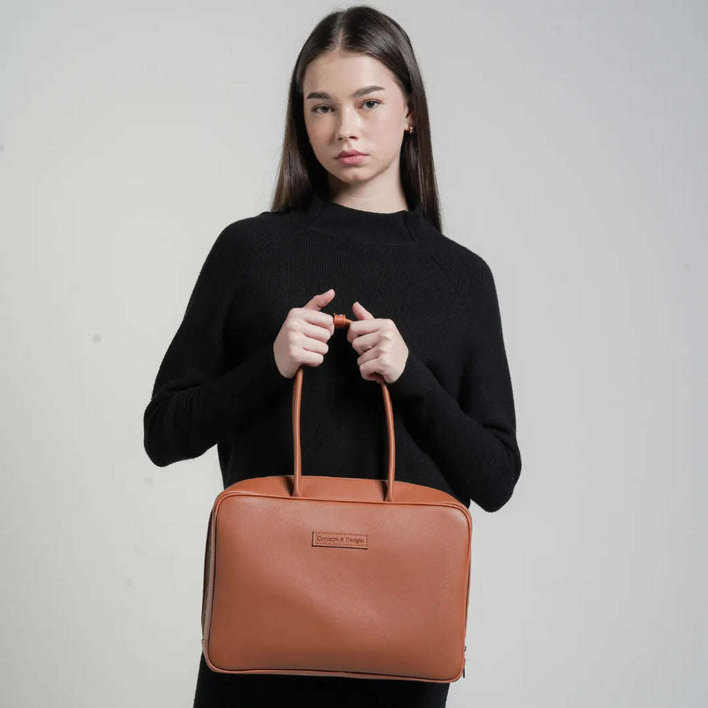 Woman holding a brown leather handbag against a plain background
#color_tan