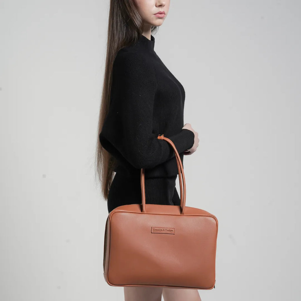 Woman holding a brown leather handbag against a plain background
#color_tan