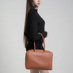 Woman holding a brown leather handbag against a plain background
#color_tan
