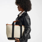 Person holding a beige tote bag with black accents on a white background
#color_malibu