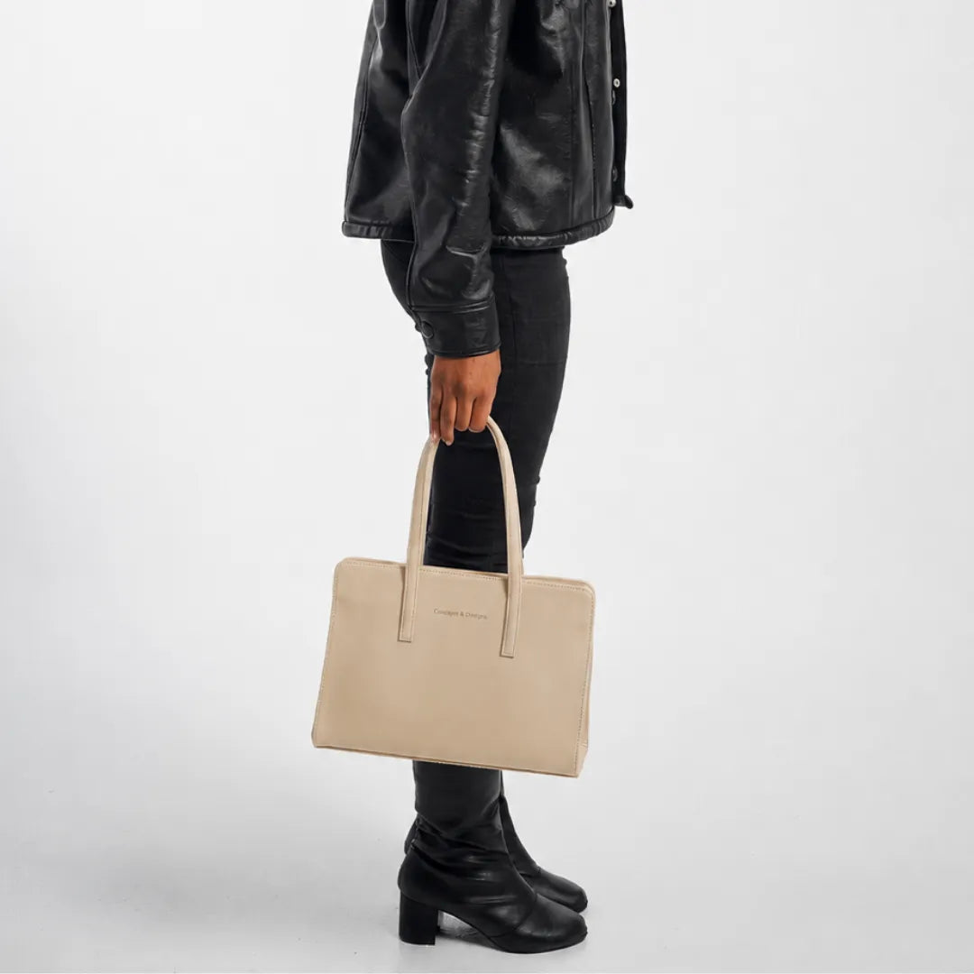 Person wearing a black leather jacket and holding a beige handbag on a white background
#color_light beige