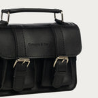 Black satchel bag with gold buckles on a light gray background
#color_midnight