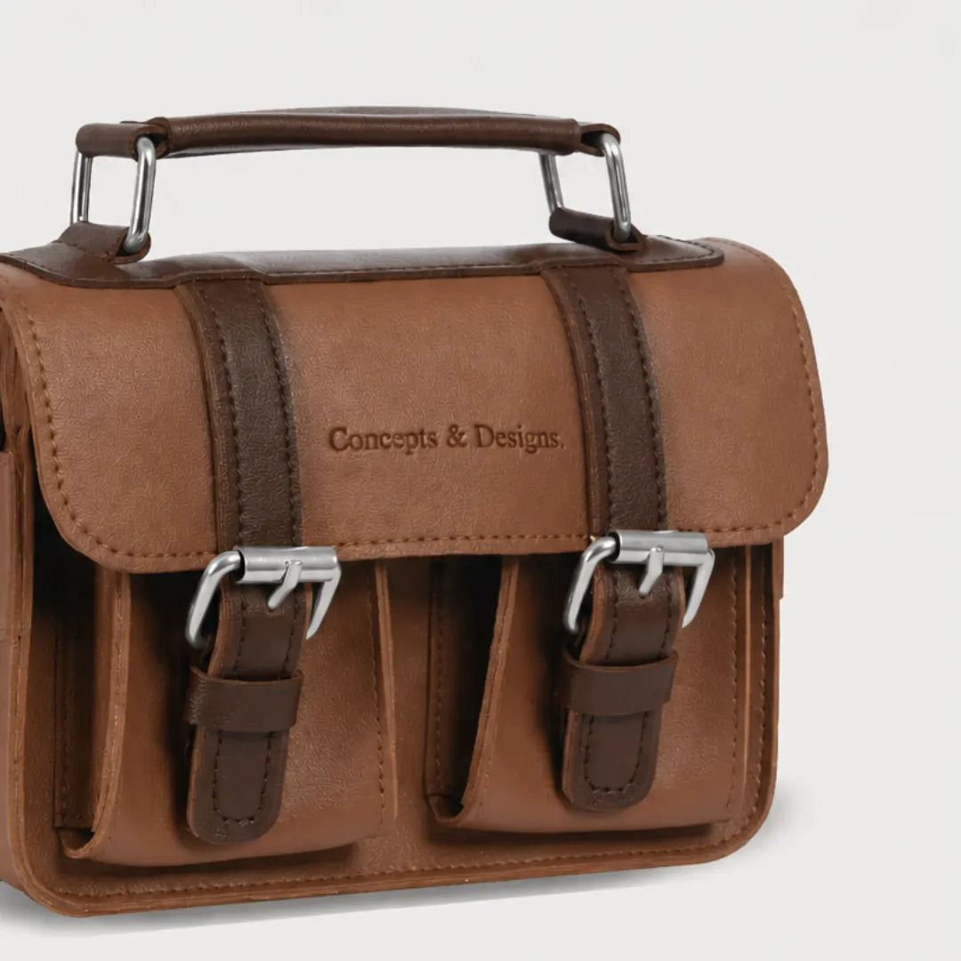 Brown leather satchel bag with metal buckles on a light gray background
#color_umber